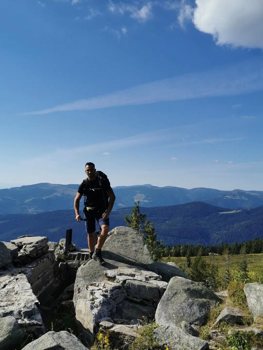 Juan sac au dos sur un promontoire rocheux, crêtes et forêts à perte de vue derrière lui