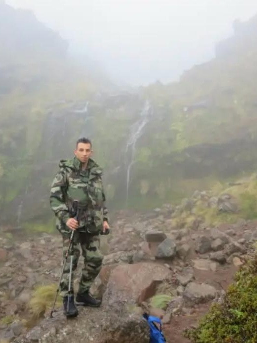 Juan en treillis, bâtons de marche à la main, dans un ravin embrumé parcouru de cascades