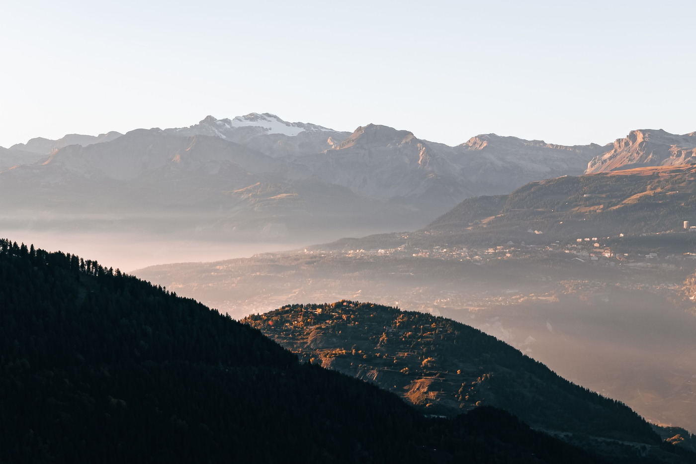 Les Alpes valaisannes au petit matin : un sommet enneigé au-dessus de crêtes ambrées, une vallée noyée dans la brume et un village accroché au versant