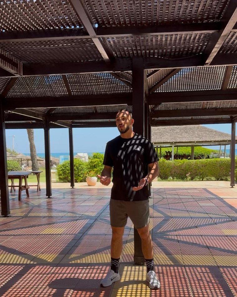 Sous une pergola en bois, l'ombre du claustra dessine un damier sur la mosaïque, la mer au fond